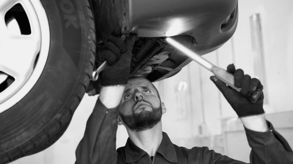 A mechanic inspects a car's underbody in a workshop, showcasing repair skills.