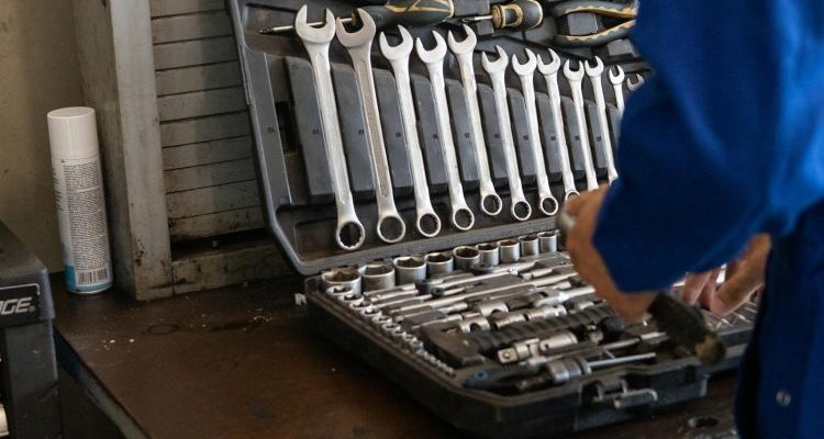 Mechanic in blue overalls organizing a toolset in an industrial workshop.